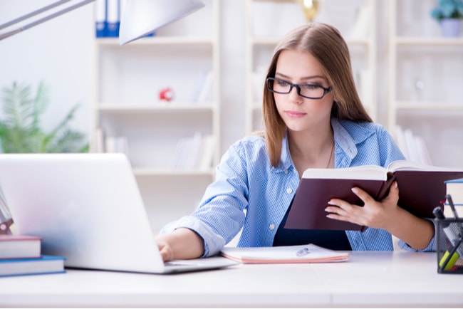 tonåring med bok framför laptop i hemmet
