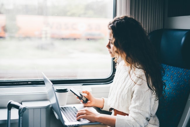 kvinna sittr på tåg och arbetar med laptop och mobil