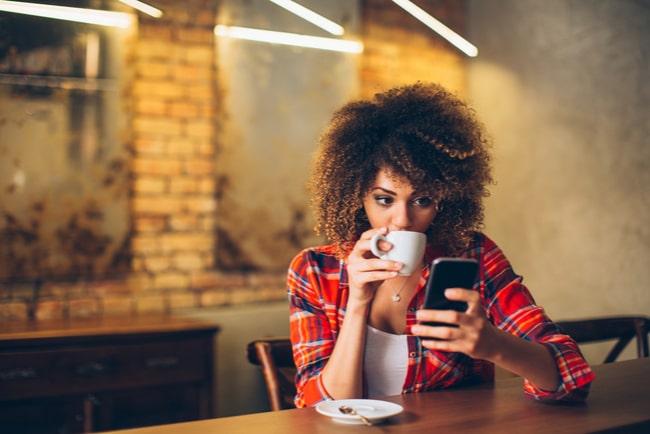 Kvinna sitter med mobil och kaffekopp på ett kafé.