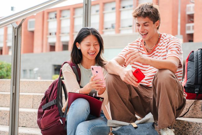 Ett par sitter i trappa med sina mobiler och skrattar.