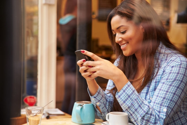 leende kvinna på café med smartphone i handen